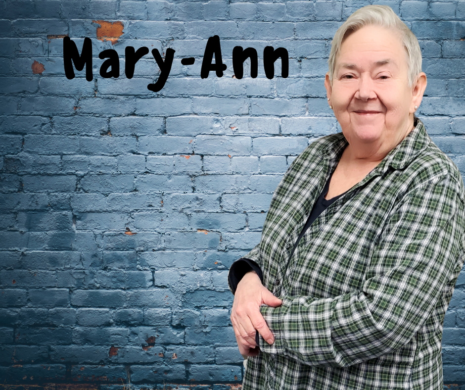 Finger Lakes Independence Center Mary-Ann in front of a blue brick wall with first name in black letters